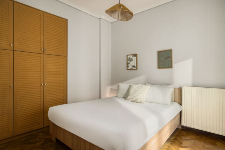 halu! Cozy bedroom with a comfortable double bed white linens and wooden furniture. Natural light fills the space creating a warm and inviting atmosphere in a modern design.